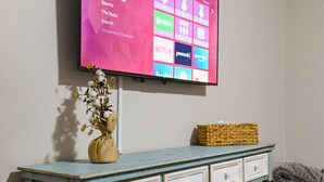 Een flatscreen televisie aan een muur, waarop een startscherm met diverse streamingdiensten wordt weergegeven.