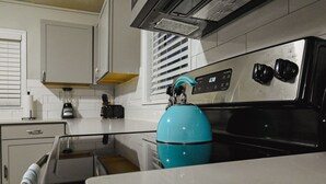 Een keuken met witte kastjes, een zwarte kookplaat en een blauwe waterkoker.