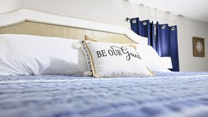 Een bed met een blauwe spreidek en witte kussens, inclusief een kussen met de tekst "BE OUR Guest".