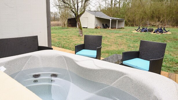 Een hottub met twee rieten stoelen, een tuinhuis en een gazon.