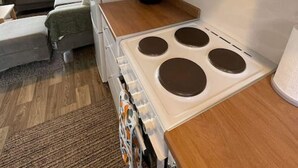 Pieni, käytännöllinen keittiönurkkaus, jossa on liesi, kahvinkeitin ja ikkuna, josta avautuu näkymä asuinalueelle.