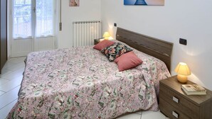 Un dormitorio con colcha estampada, cabecera de madera, dos lámparas de noche y una mesita de noche con un libro.