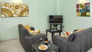 Una sala de estar con dos sofás grises, una mesita negra con una botella de vino y una copa, y un televisor de pantalla plana sobre un mueble.