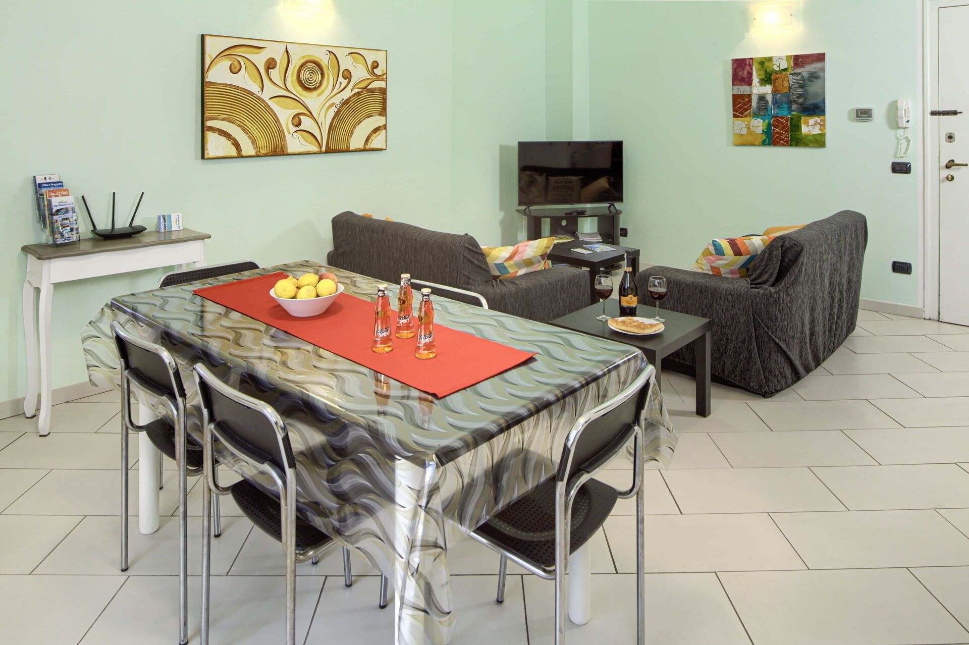 Un coin repas avec une table dressée pour quatre personnes, un canapé, un téléviseur et un petit meuble agrémenté d’une plante.