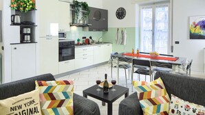 Una cocina moderna con armarios blancos, un comedor con mesa y sillas, y un sofá con cojines estampados.