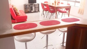 A dining area with a wooden table, red placemats, and white bar stools. - apartamento bahía fragata  (San Andrés)