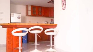 A kitchen with wooden cabinets, a white refrigerator, and three white bar stools. - apartamento bahía fragata  (San Andrés)