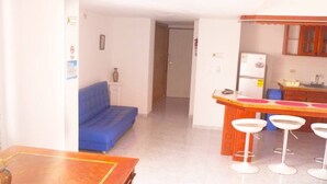 A compact living space with a kitchenette, a blue sofa, and a small dining area with stools. - apartamento bahía fragata  (San Andrés)