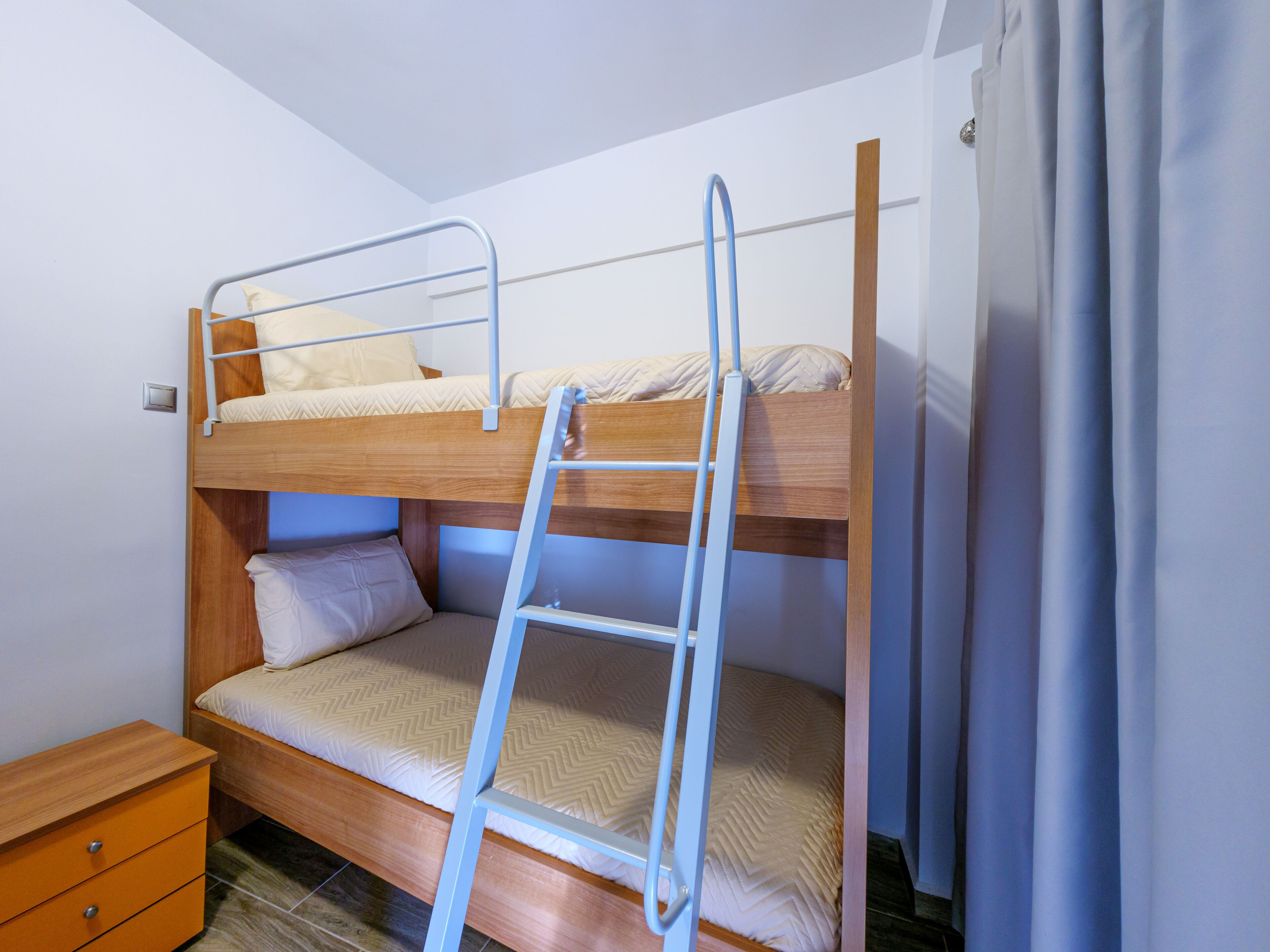 A bunk bed with a ladder, a wooden nightstand, and a curtain.