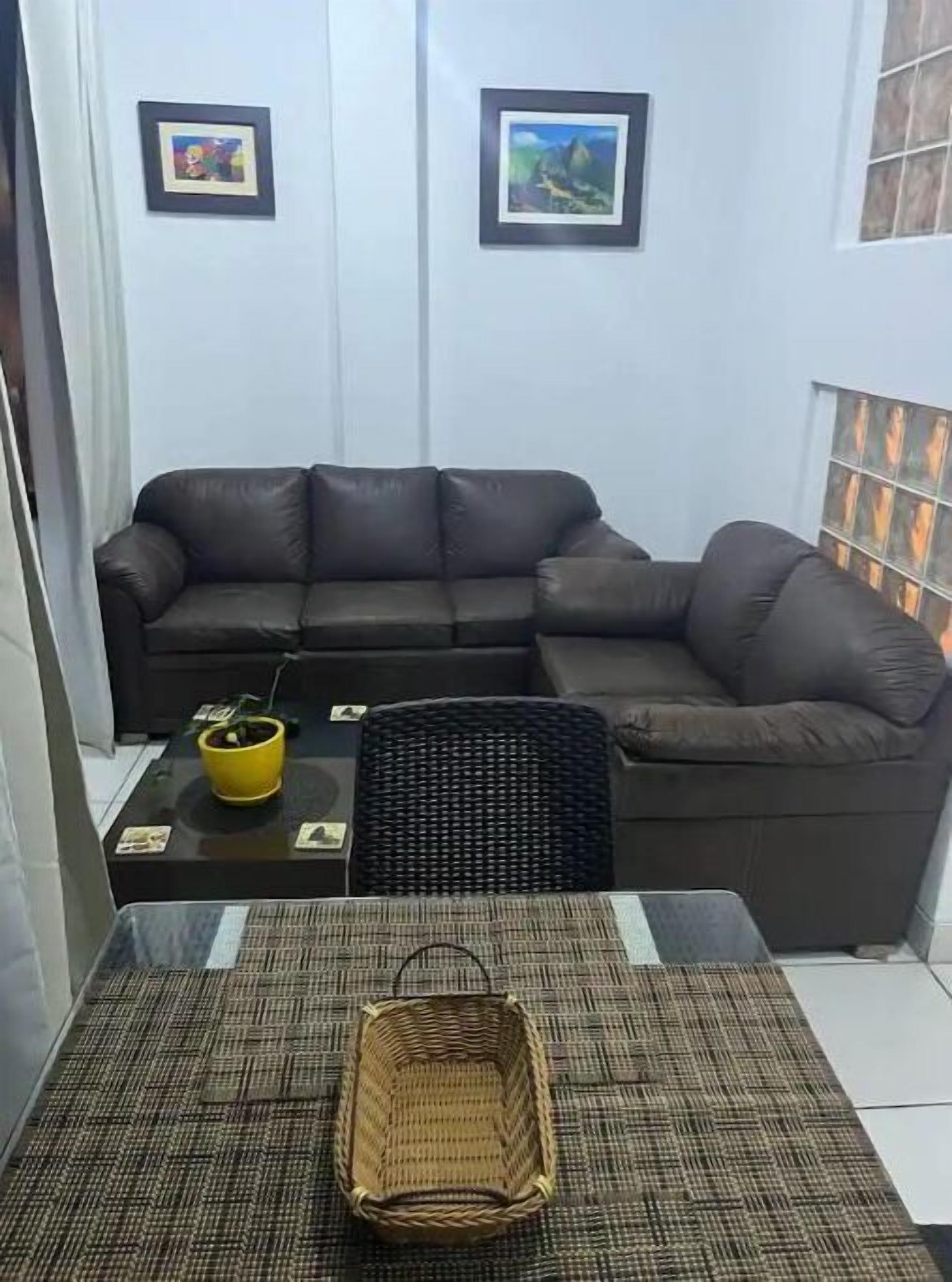 A living room with a brown leather sofa, a small table with a yellow pot, and a woven basket on a patterned mat.