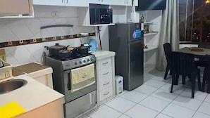 Uma cozinha moderna com armários brancos, fogão, geladeira e um espaço de refeições com mesa e cadeiras.
