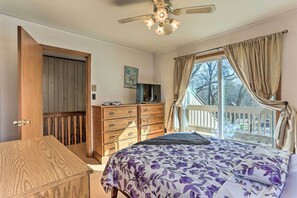 Quarto com cama, cómoda de madeira, televisão e varanda com cortinas.