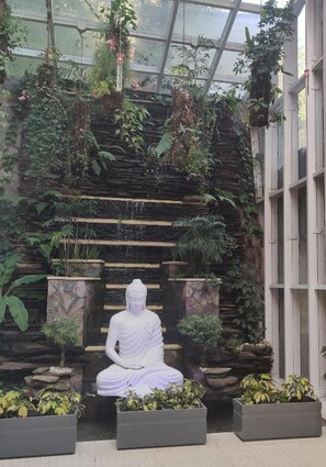 Un jardín interior tranquilo con una estatua de Buda, abundante vegetación y un fondo de pared de piedra.