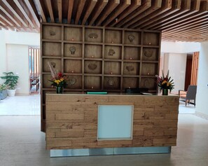 A reception desk with a wooden panel design, a glass panel on the front, and a ceiling with wooden beams. - Yog Wellness Resort & Spa by Amritara (Dehradun)
