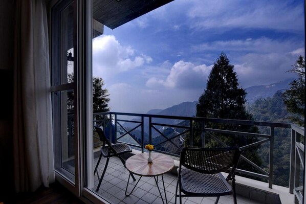 A balcony with a table and chairs, overlooking a mountainous landscape.