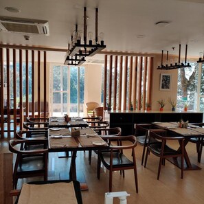 Un comedor con sillas y mesas de madera, ventanas amplias y una lámpara de araña moderna.