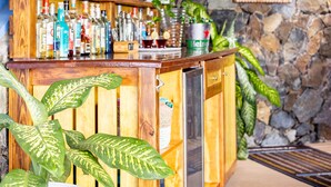 A bar area with wooden shelves stocked with various bottles, a dartboard on the wall, and a stone wall backdrop. - Blue Moon Villa (Tortola)