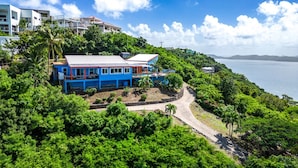 A coastal property with a prominent blue house, lush greenery, and a clear view of the sea. - Blue Moon Villa (Tortola)