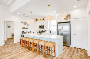 A modern kitchen with a central island, bar stools, stainless steel appliances, and pendant lighting.