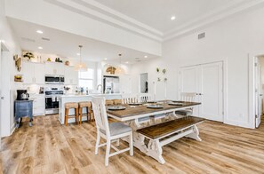 A spacious kitchen with white cabinetry, a central island, and a dining area with a wooden table and white chairs.