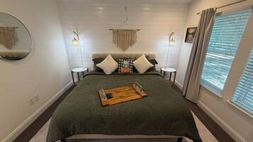 A bedroom with a bed, bedside tables, a mirror, and a window with curtains.