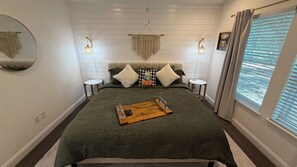 Un dormitorio con una cama, mesitas de noche, un espejo y una ventana con cortinas.