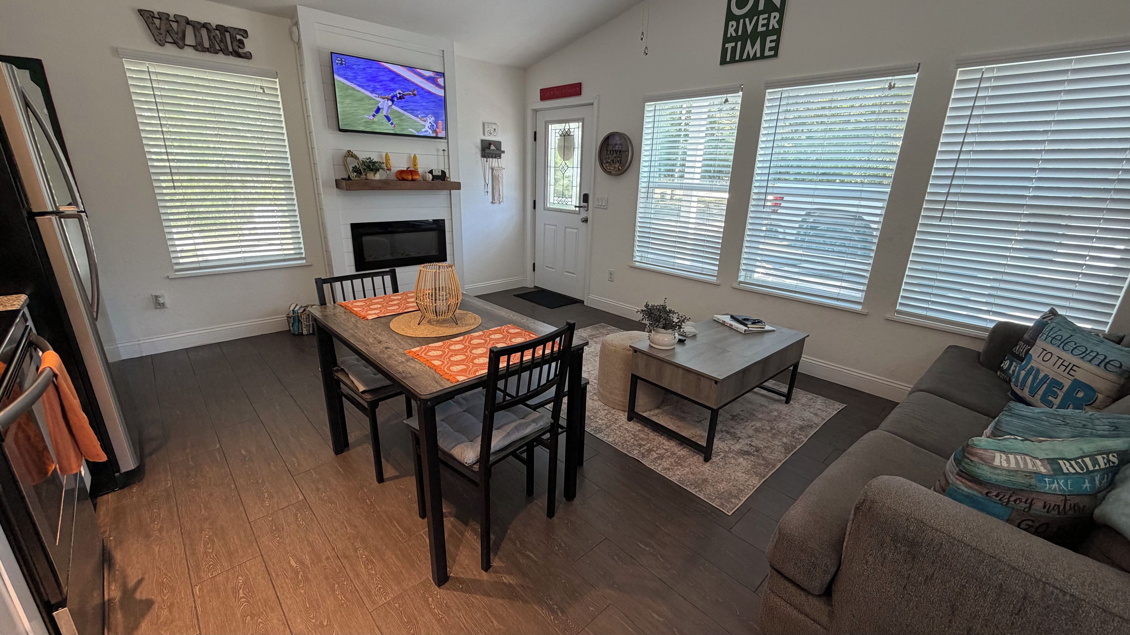 A living room with a TV, a fireplace, a dining area with a table and chairs, and a couch with decorative pillows.
