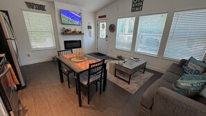 Una sala de estar con televisor, chimenea, comedor con mesa y sillas, y sofá con cojines decorativos.
