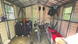 A covered storage area with bicycles, paddles, and a red kayak.
