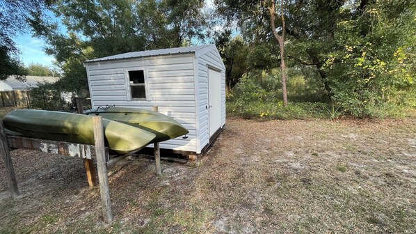 Eine kleine, einstöckige Holzhütte mit Tür und Fenster, gelegen in einem bewaldeten Gebiet, mit einem Boot, das an einem Holzpfosten lehnt.