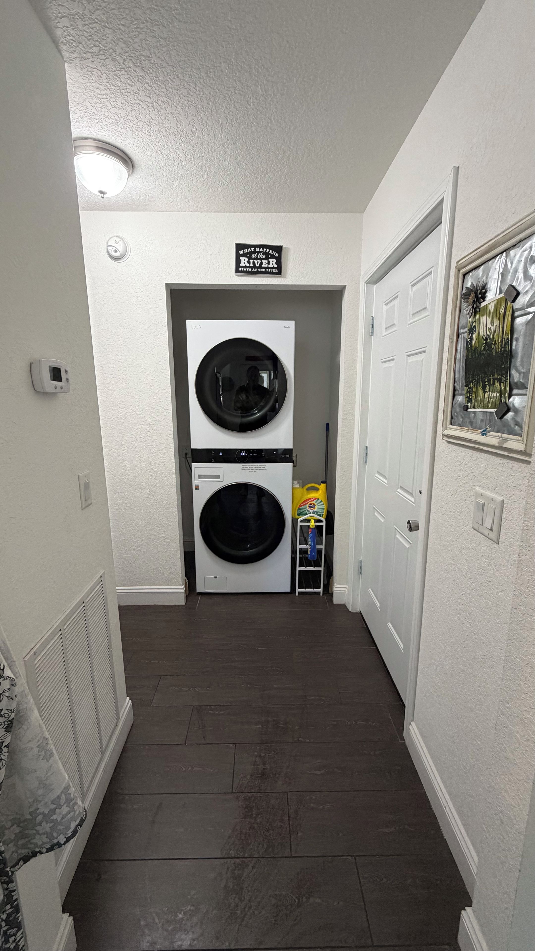 A laundry room with two stacked front-loading washers and dryers, a sign above them, and a door to the right.