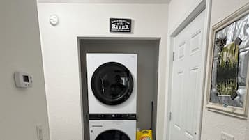 A laundry room with two stacked front-loading washers and dryers, a sign above them, and a door to the right.