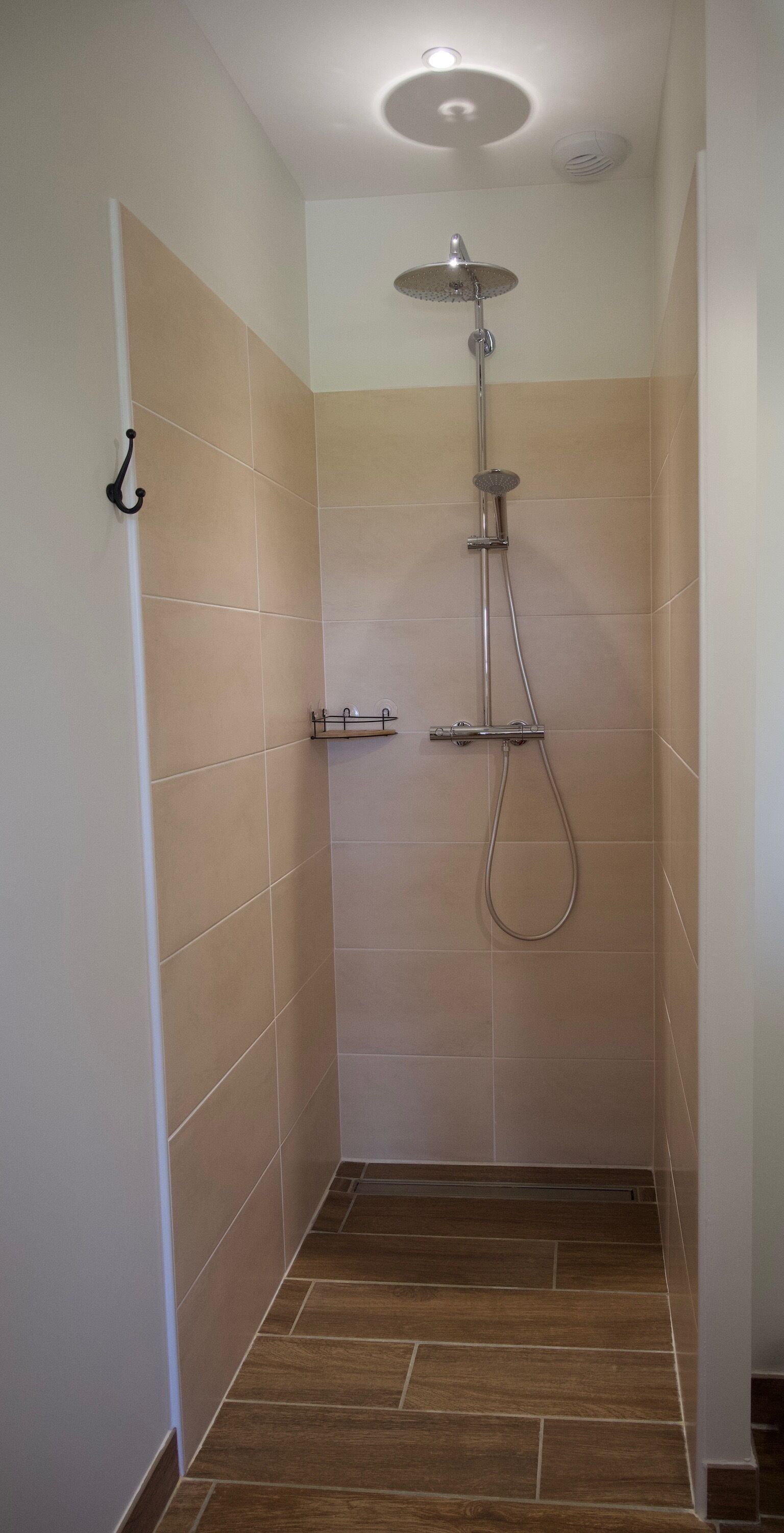 Une petite salle de douche carrelée, équipée d’un pommeau de douche à main et d’un pommeau de douche fixé au mur.