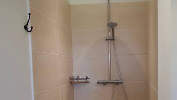 Une petite salle de douche carrelée, équipée d’un pommeau de douche à main et d’un pommeau de douche fixé au mur.