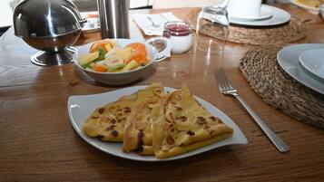 Een houten tafel met een stapel pannenkoeken, een schaal fruitsalade en een thermoskan.