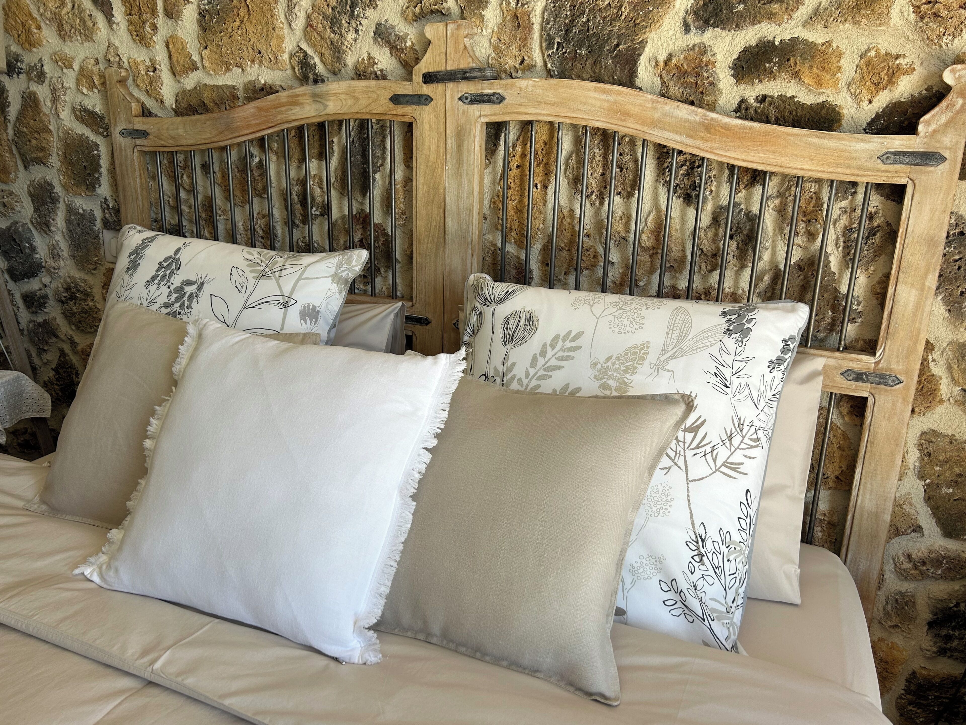 A bed with a stone wall backdrop, featuring a wooden headboard with vertical slats and floral-patterned pillows.