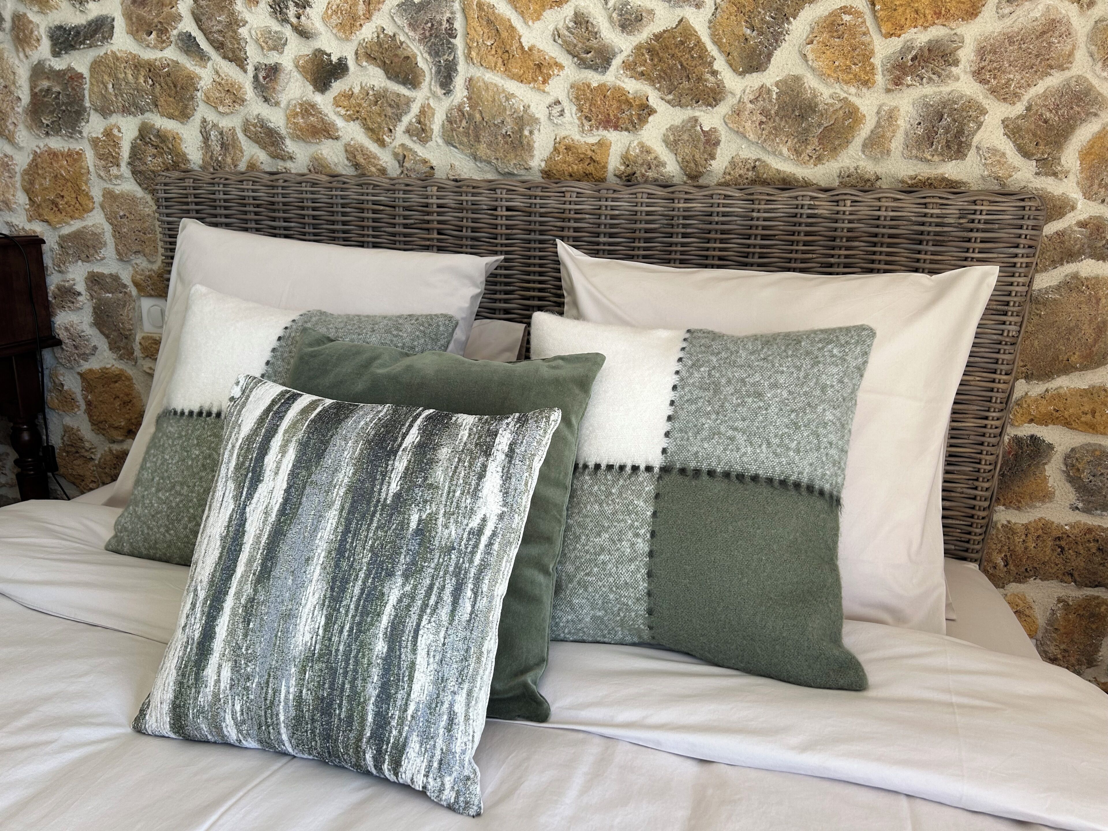 Ein Bett mit einer Steinsandsteinwand im Hintergrund, einem Rattan-Kopfstück und mehreren Kissen.