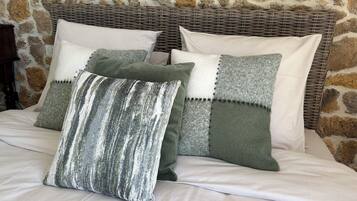Ein Bett mit einer Steinsandsteinwand im Hintergrund, einem Rattan-Kopfstück und mehreren Kissen.