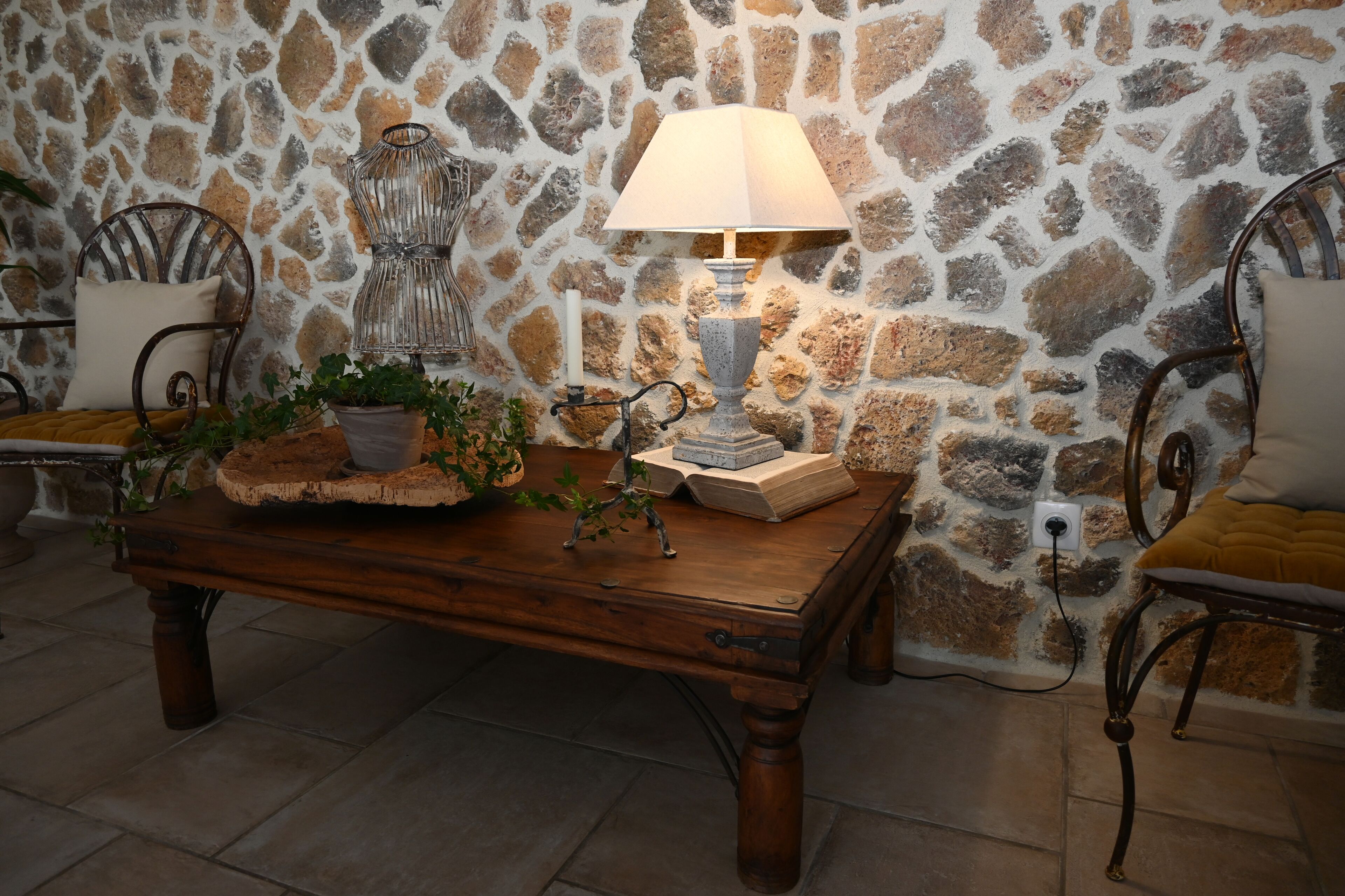 Una mesa de madera con una lámpara, libros y una planta en maceta frente a una pared de piedra.