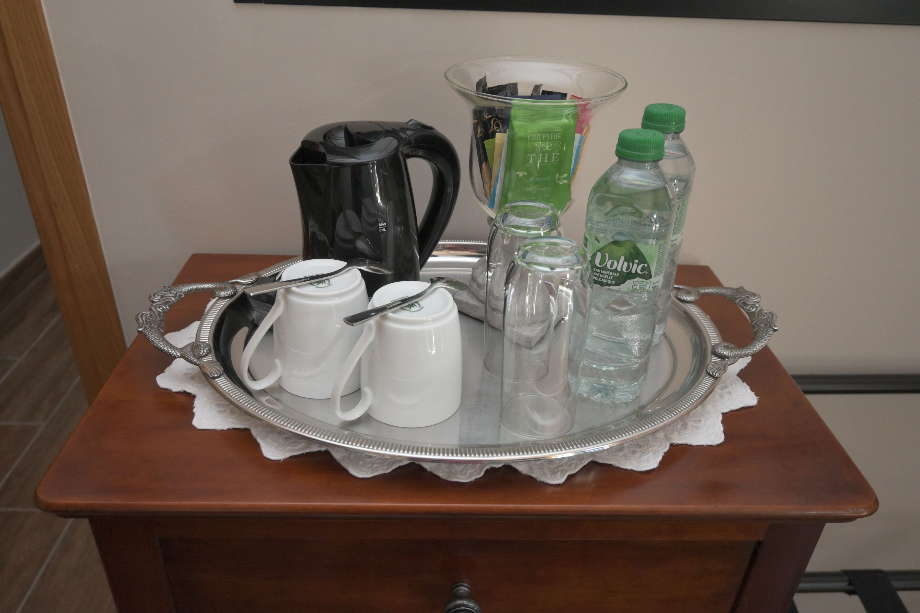 A tray with a coffee maker, teapots, cups, a glass pitcher, and bottles on a wooden table.