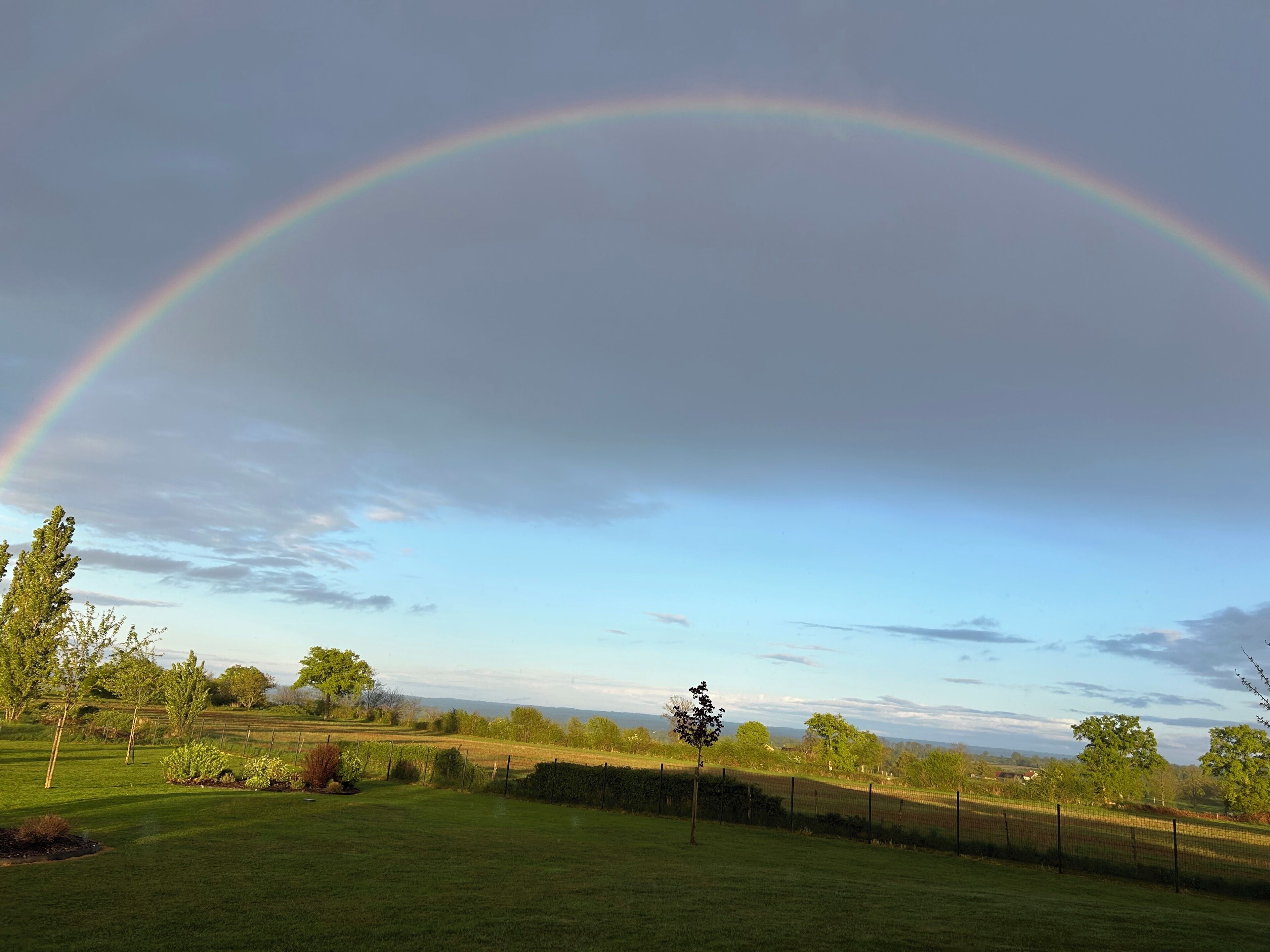A landscape with a rainbow arching across the sky, a grassy field, and a distant tree line.