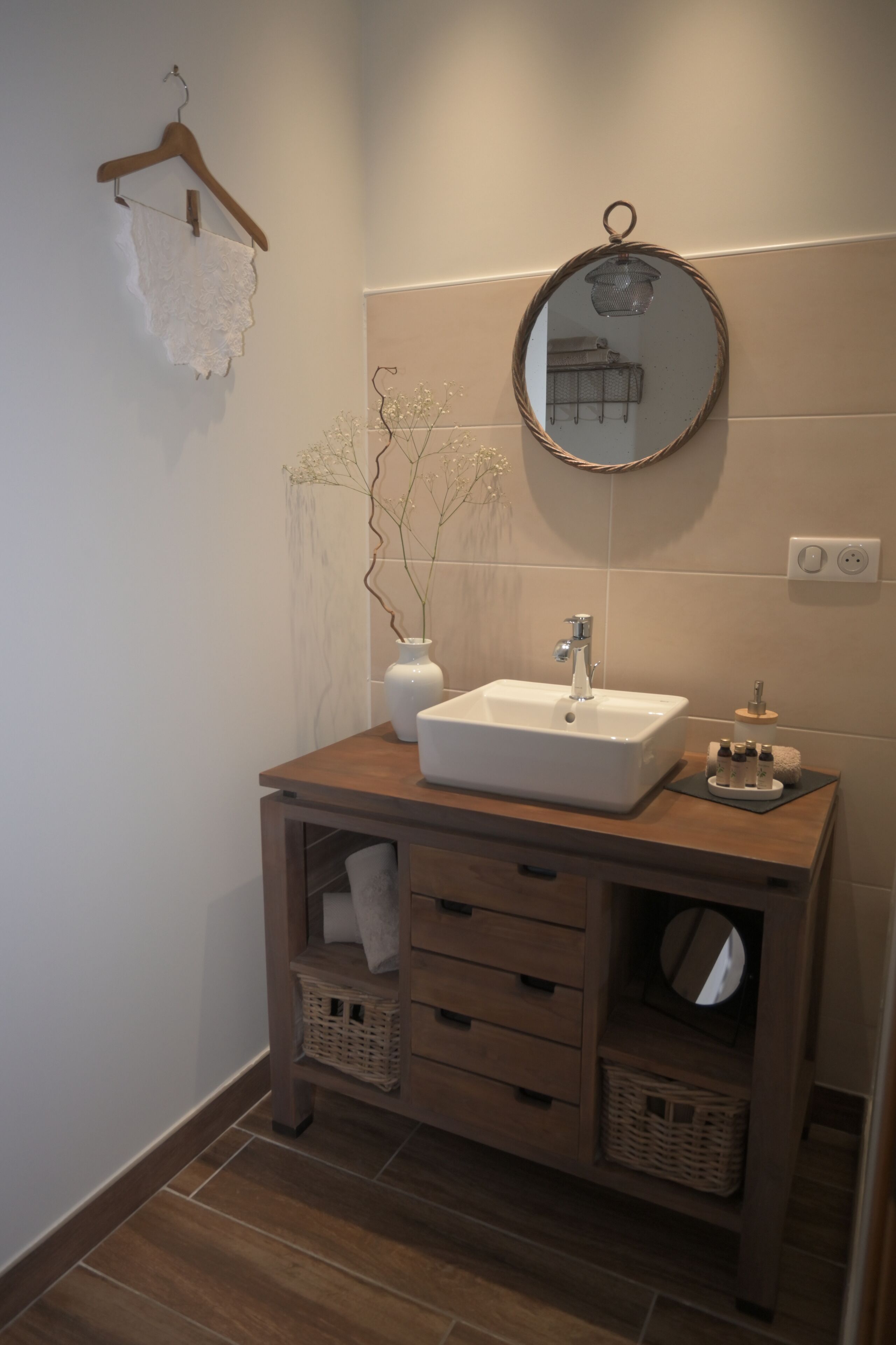 A bathroom with a wooden vanity, a white sink, a mirror, and a vase with branches.
