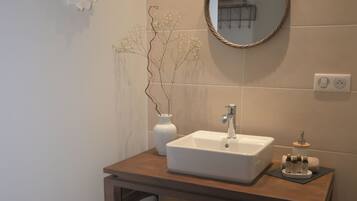 A bathroom with a wooden vanity, a white sink, a mirror, and a vase with branches.