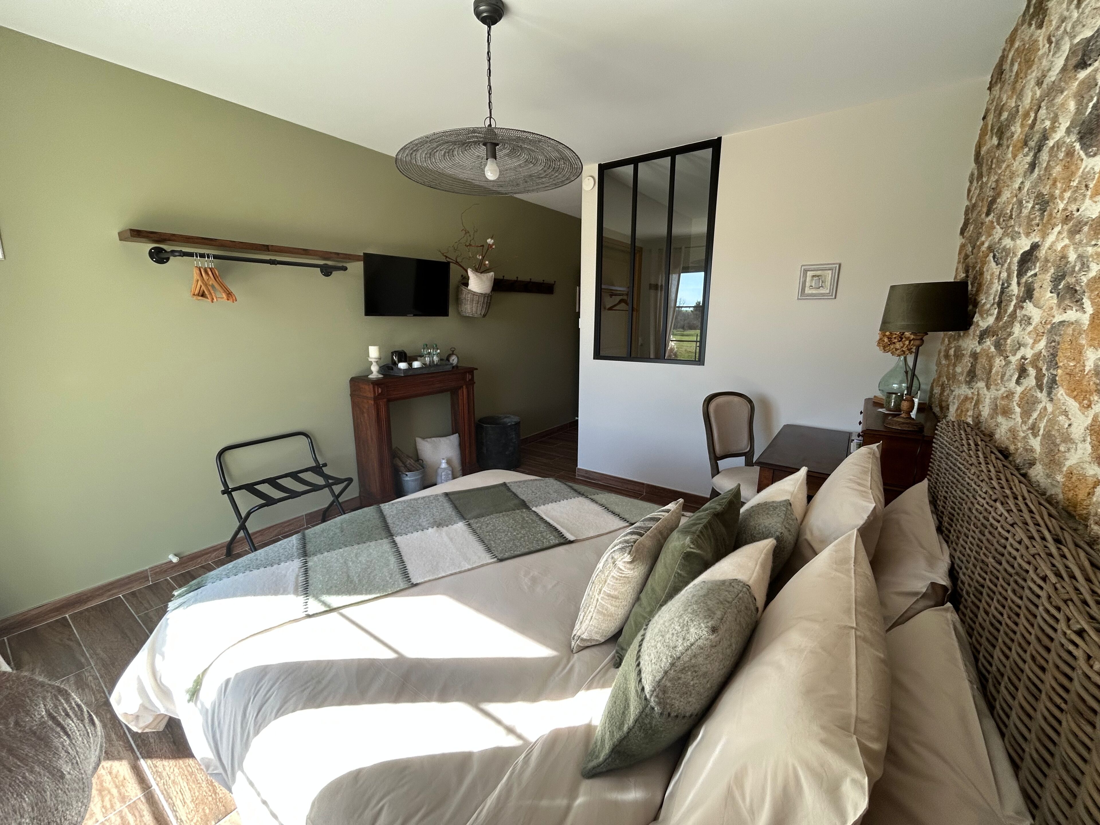 A bedroom with a large bed, a desk, a chair, a television, and a window.