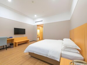 Una habitación de hotel moderna con una cama grande, un escritorio con silla, un televisor montado en la pared y un baño pequeño visible a través de una puerta abierta.