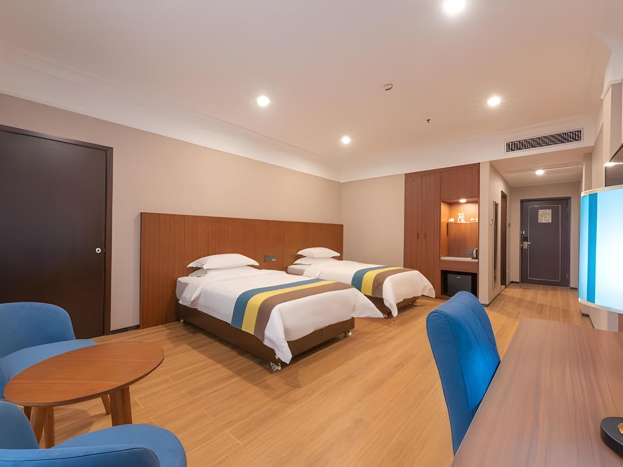 A hotel room with two beds, a wooden headboard, a small table, and a blue armchair.