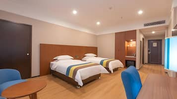 A hotel room with two beds, a wooden headboard, a small table, and a blue armchair.