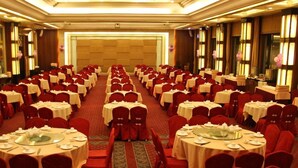 Un salón de banquetes con mesas redondas y sillas rojas, dispuestas en filas.