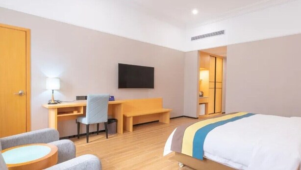 Habitación de hotel con cama, escritorio, silla, televisor y una mesita.