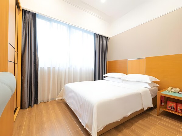 Una habitación de hotel con una cama grande, cabecera de madera, mesita de noche con teléfono y una ventana con cortinas.